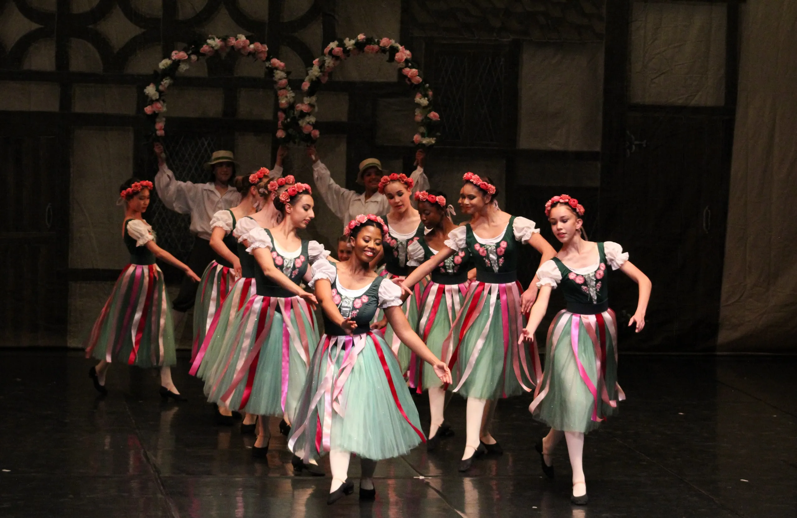 Dancers perform as a large group as part of YRBC's 2024 production of Coppelia. The dancers are dressed in green skirts with pink ribbons and are wearing flower crowns.